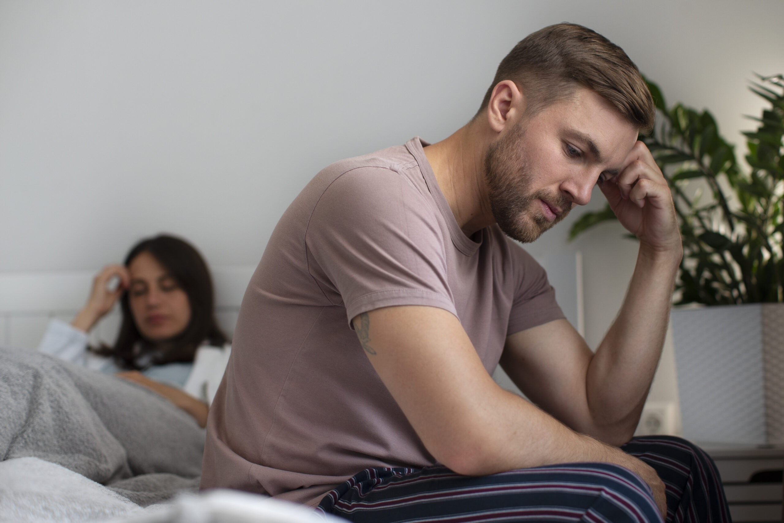 Upset man sitting on the edge of the bed after an argument with his partner, reflecting relationship stress or emotional conflict