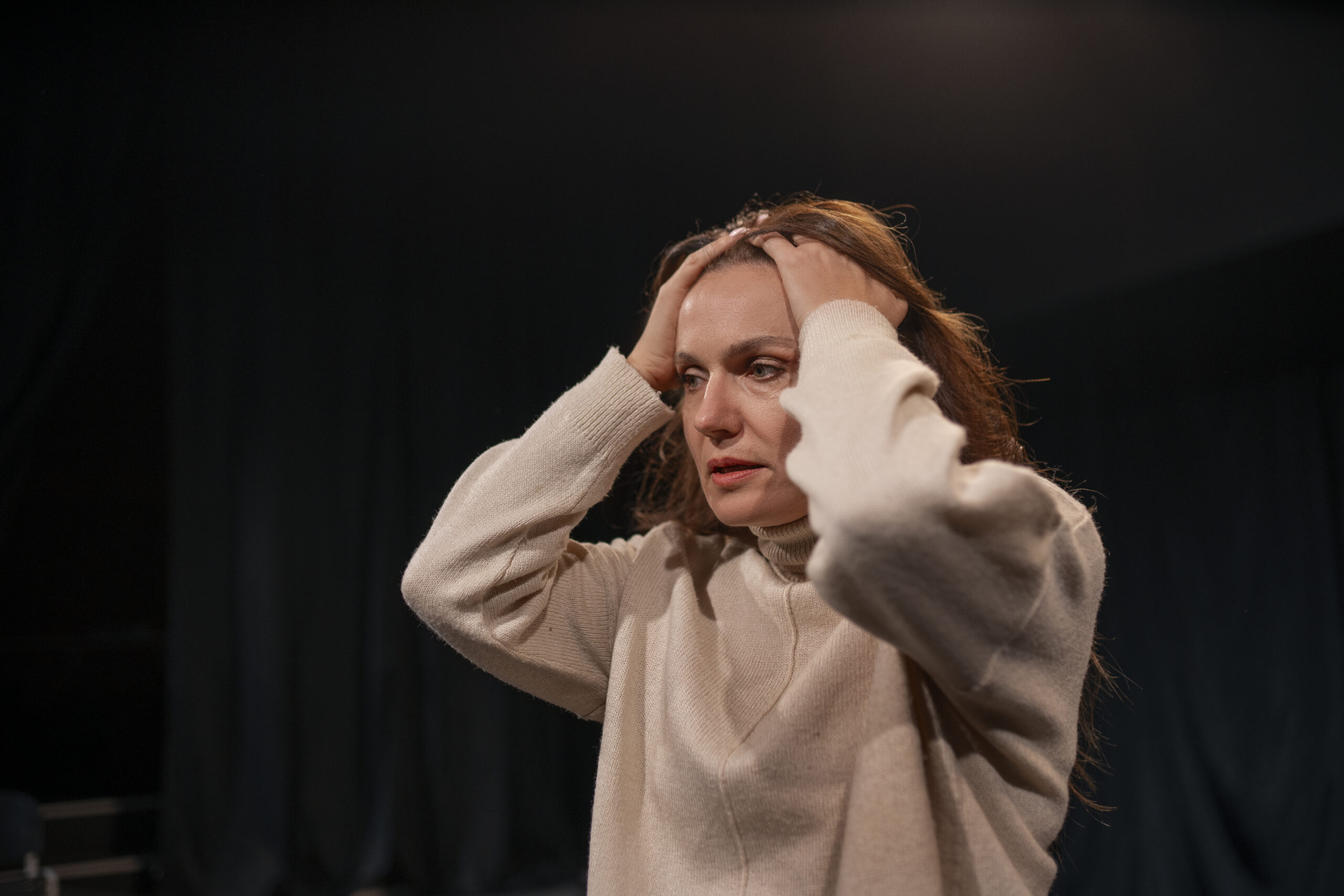 Woman holding her head in distress, showing signs of stress or anxiety in a dark room