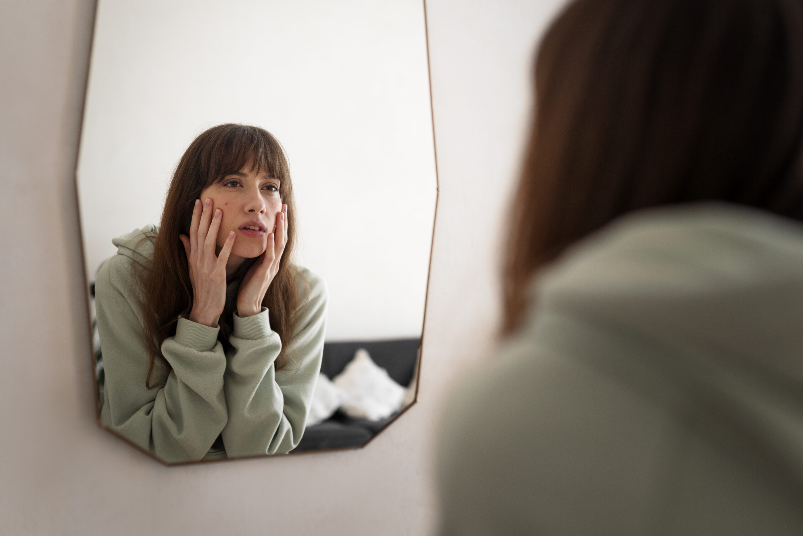 Woman looking at herself in the mirror with a worried expression, reflecting low self-esteem or lack of confidence
